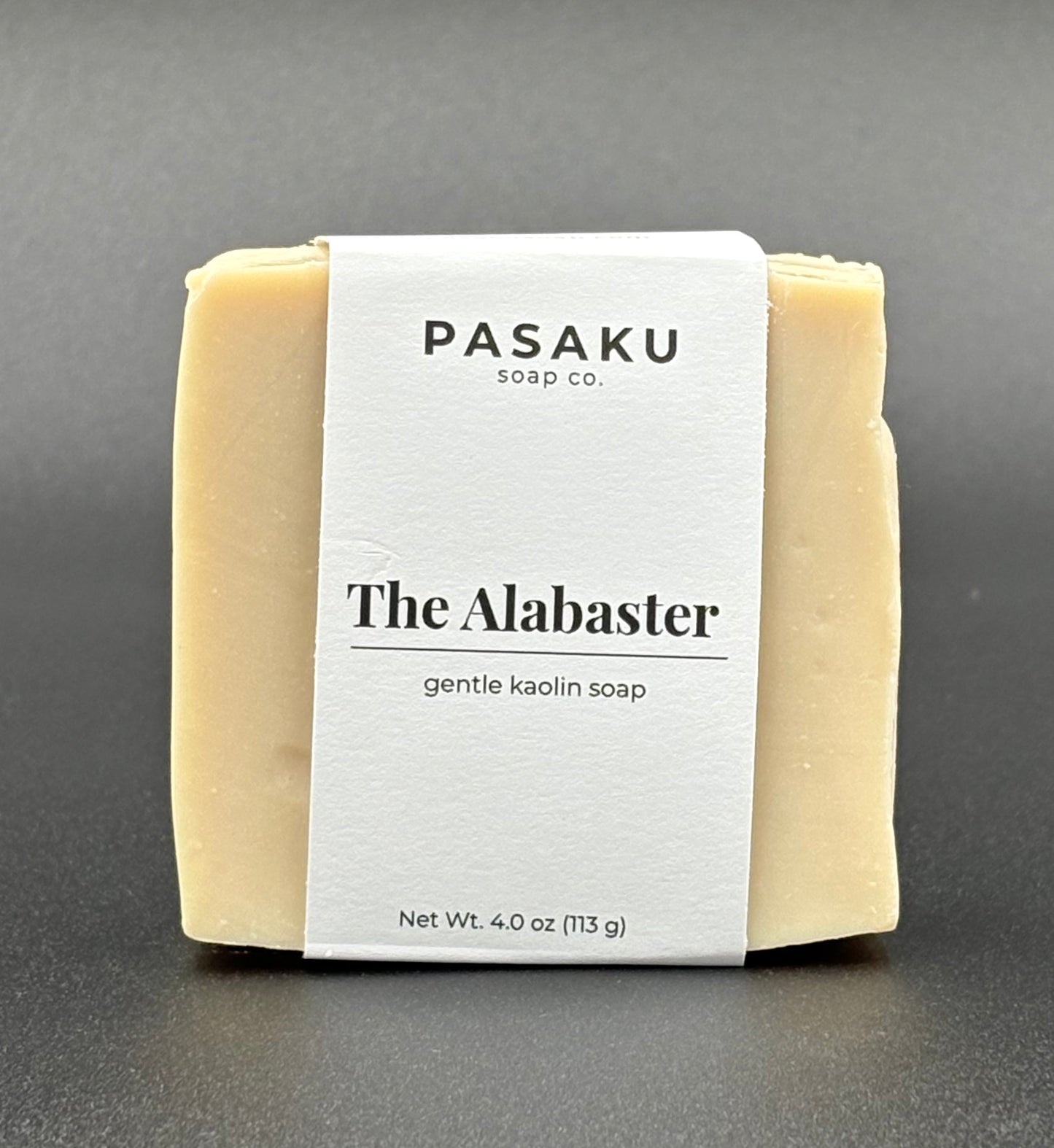 Pasaku Alabaster  white kaolin soap bar, with white wrap around label that has the name of the company, the name of the soap, and the net weight of 4 oz.