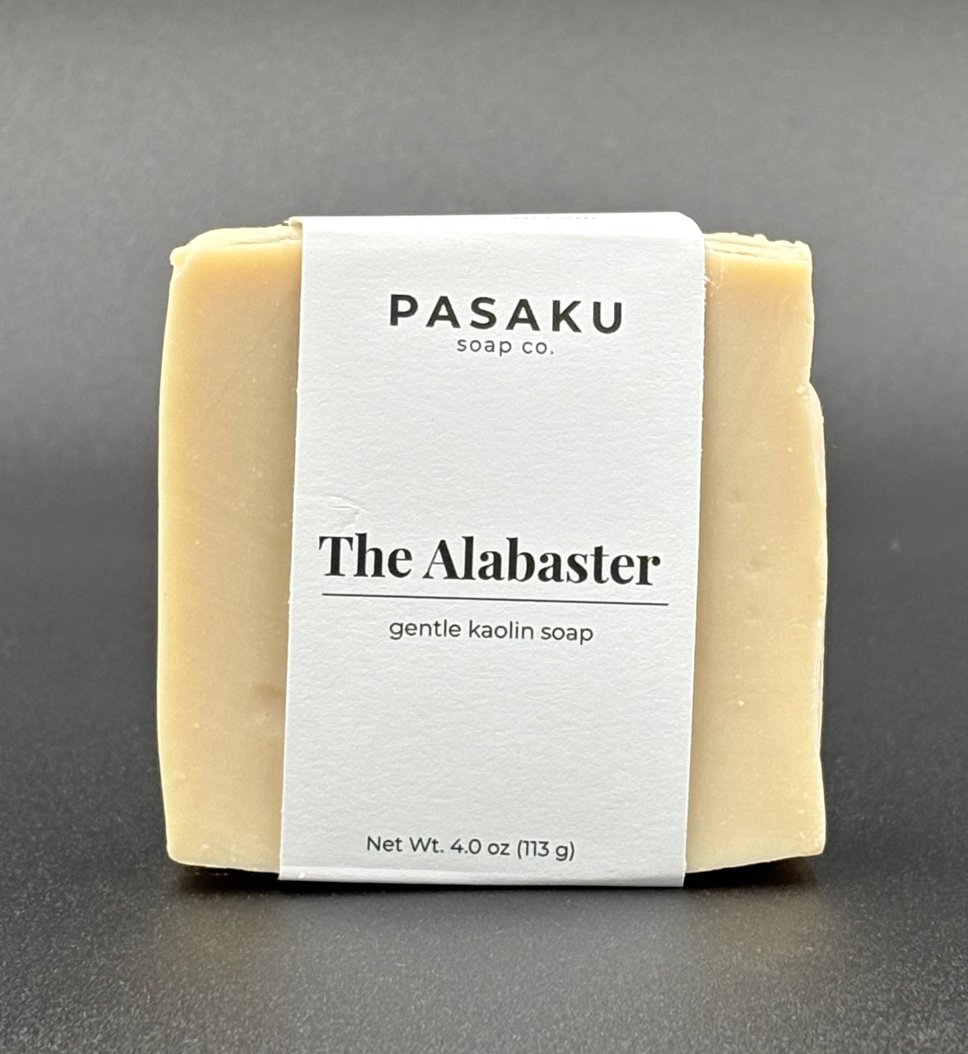 Pasaku Alabaster  white kaolin soap bar, with white wrap around label that has the name of the company, the name of the soap, and the net weight of 4 oz.