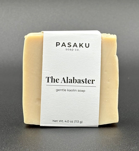 Pasaku Alabaster  white kaolin soap bar, with white wrap around label that has the name of the company, the name of the soap, and the net weight of 4 oz.